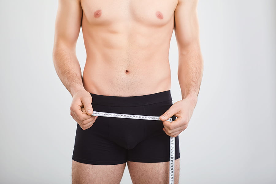 A man in underwear holds a centimeter in his hands measures the penis.